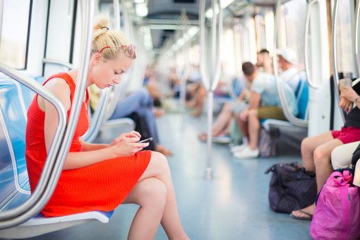 Beautiful blonde caucasian lady in red dress traveling by metro.