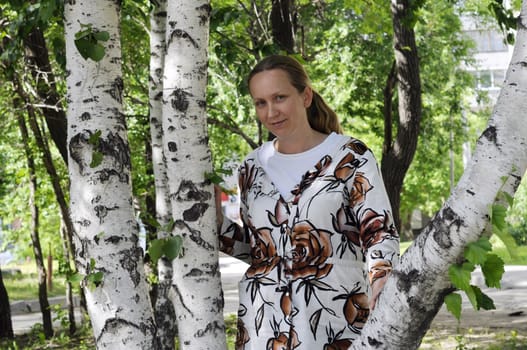The happy woman stands near birches in park