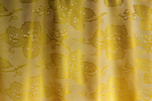  Beautifully draped silk fabric of golden color with an ornament. . It is presented as the background image.