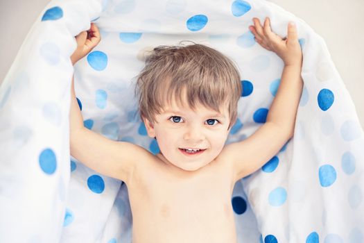 smiling little boy holding blanket after sleeping, shallow DOF