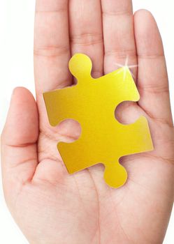 Hand holding a gold jigsaw piece 