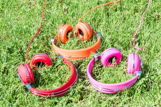 Three varicolored vibrant colorful headphones on summer sunlit green fresh lawn