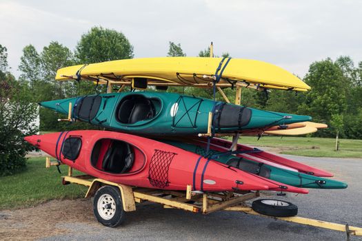 Trailer full of six colorful one man kayaks in a parking lot. 