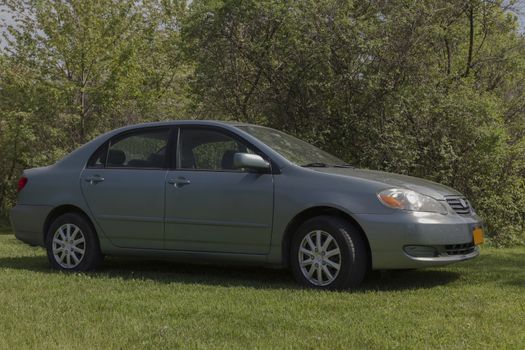 Four door compact car in green. Made in 2005. Parked in a grass yard. 