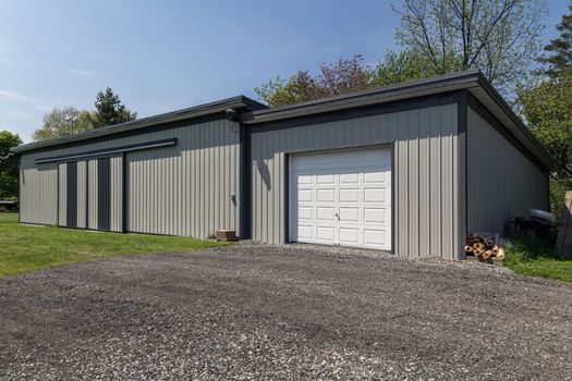 Large grey steel barn in modern style. White garage door with gravel driveway. 