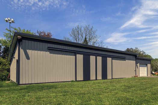 Long steel and modern barn with closed sliding doors and garage addition. Blue sky in the background. 