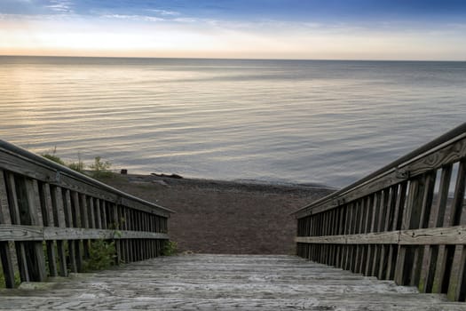Wide wooden stairway to small beach on the lakefront. Calm water and sky in the background.