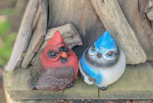 Cartoon style cardinal and bluejay statue on top of a wooden birdhouse. 