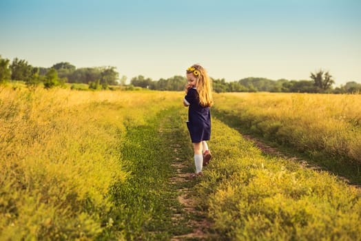 the beautiful little girl in a blue dress laughs, holds hands at the person, looking back, goes to a field