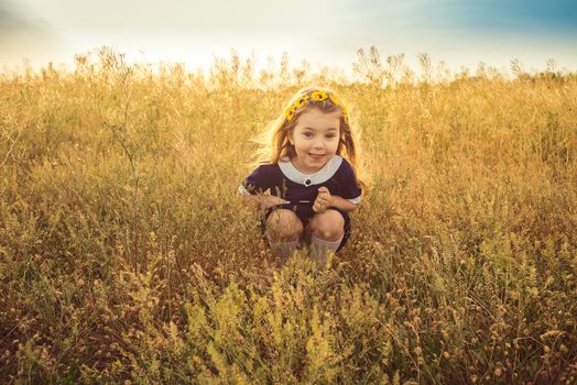 the beautiful little girl in a blue dress sitting in the field smiles