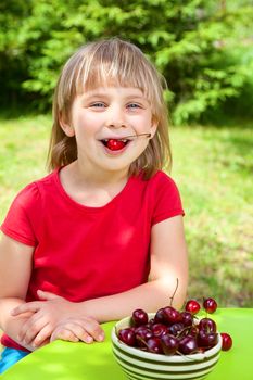 Cute little girl eating sweet cherry outdoors