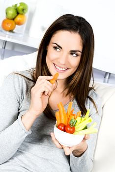 Woman eating salad. Beautiful healthy smiling Caucasian woman enjoying a fresh healthy salad sitting in sofa looking up. High angle view with copy space on modern interior. 