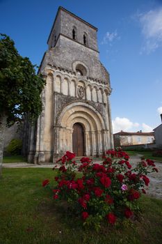 Facade of the romanesque Rioux church with red  roses in the forefront. Region of Charente in France