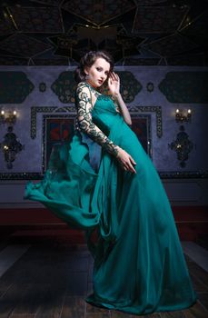 Beautiful woman in a green long dress on a background of richly decorated room