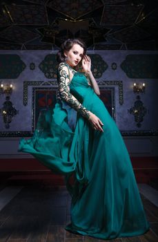 Beautiful woman in a green long dress on a background of richly decorated room