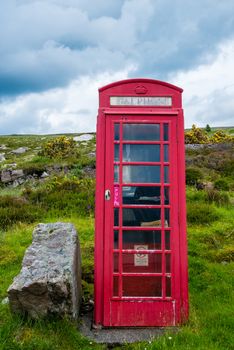 Old-fashioned traditional red telephone booth or public payphone standing next to an open deserted field in Scotland