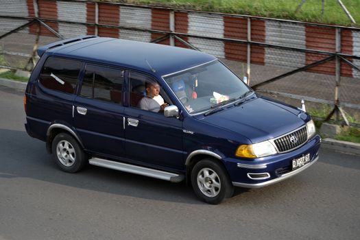 bandung, indonesia-june 16, 2014: blue colored toyota kijang EFI cruising on the road.