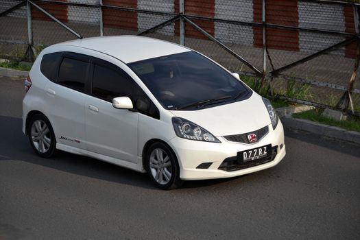 bandung, indonesia-june 16, 2014: white colored honda jazz RS cruising on the road.