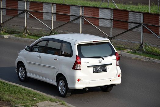 bandung, indonesia-june 16, 2014: white colored toyota avanza cruising on the road.