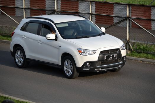 bandung, indonesia-june 16, 2014: white colored mitsubishi outlander sport cruising on the road.