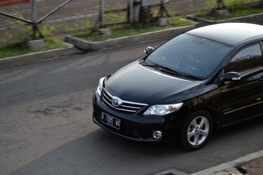 bandung, indonesia-june 16, 2014: black colored toyota corolla altis cruising on the road.