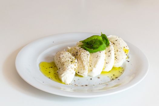 Slices of italian mozzarella with leaves of basil, olive oil and pepper