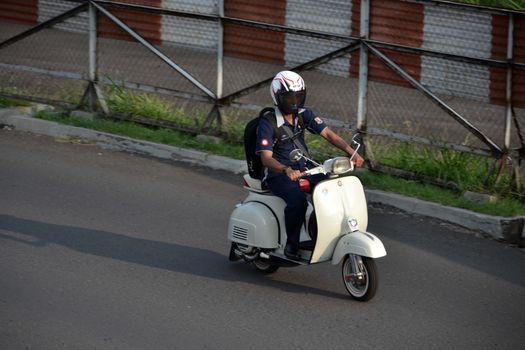 bandung, indonesia-june 16, 2014: man with backpack are riding white scooter in the afternoon.