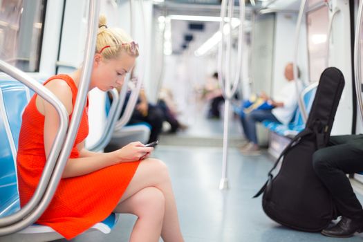 Beautiful blonde caucasian lady in red dress traveling by metro.