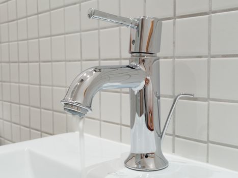 Water flowing out of a silver faucet in a bathroom handbasin