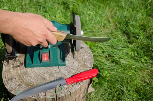 Hand grinder knives with electric tool on outdoor log.