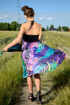 Young female model spins around. Charming girl from Poland, dynamic photo with colorful dress. Green fields and blue sky as background.