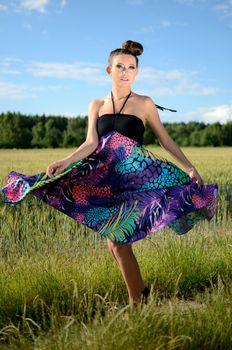 Young female model spins around. Charming girl from Poland, dynamic photo with colorful dress. Green fields and blue sky as background.