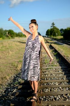 Girl with short skirt walks along railroad. Polish female model with blue sky and green meadows behind her.