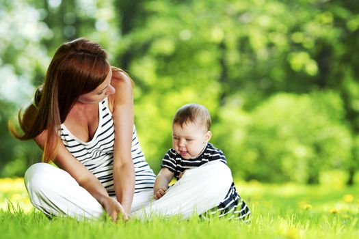 Mother and daughter sitting on grass in spring park