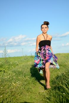 Happy girl runs with colorful dress. Active teenage model from Poland surrounded by green fields and blue sky.