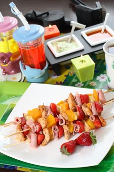 Colorful skewers of chicken, strawberries and pineapple on a white plate