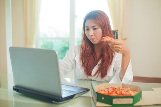 Happy asian young woman using laptop and eating pizza at home