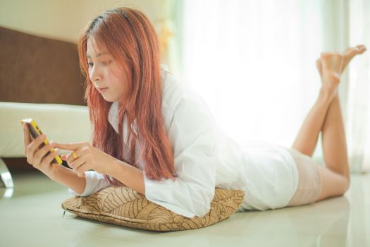 Happy asian young woman lying using smart phone at home