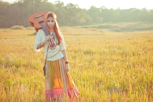 Hippie woman walking in golden field with acoustic guitar
