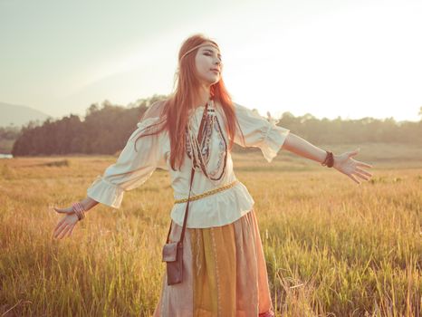 Hippie woman with arms outstretched in golden field on sunset