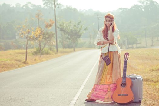 Beautiful young hippie girl using mobile phone on the country road