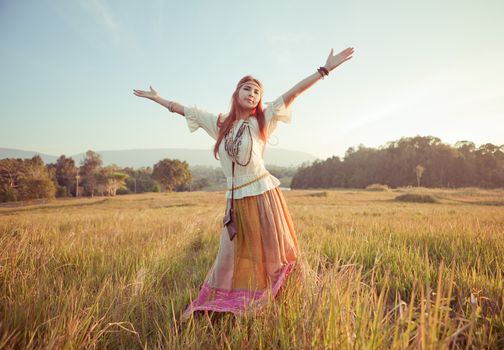 Hippie woman with arms outstretched in golden field on sunset