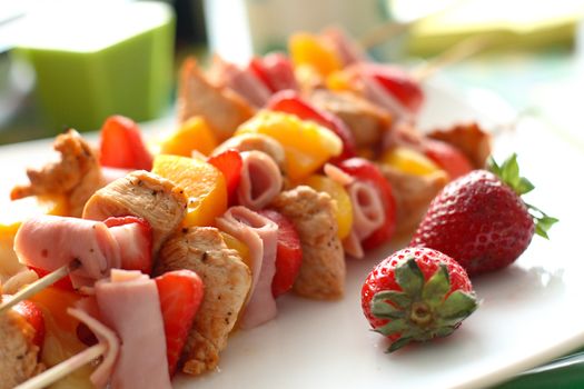 Colorful skewers of chicken, strawberries and pineapple on a white plate