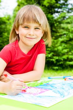 Little girl sitting at table drawing a house outdoors