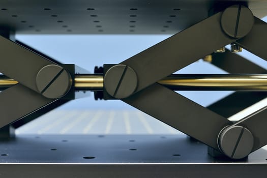 fragment of lab jack mechanism on the steel table; used in opto-mechanics and research; selective focus on front screws and axis