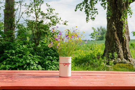 ancient vase with wild flowers standing outside on red table