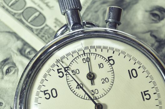 stopwatch lays over US dollar banknotes; focus on watch arrow