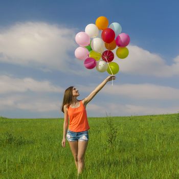 Young beautiful woman having fun with balloons on a green meadow