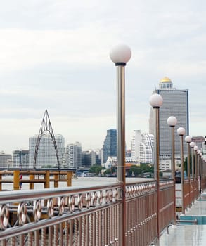 Landscaped waterfront with boat sailing in the river and tall buildings in Thailand's capital.                              