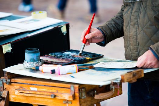 Painter with brush painting his picture on a street